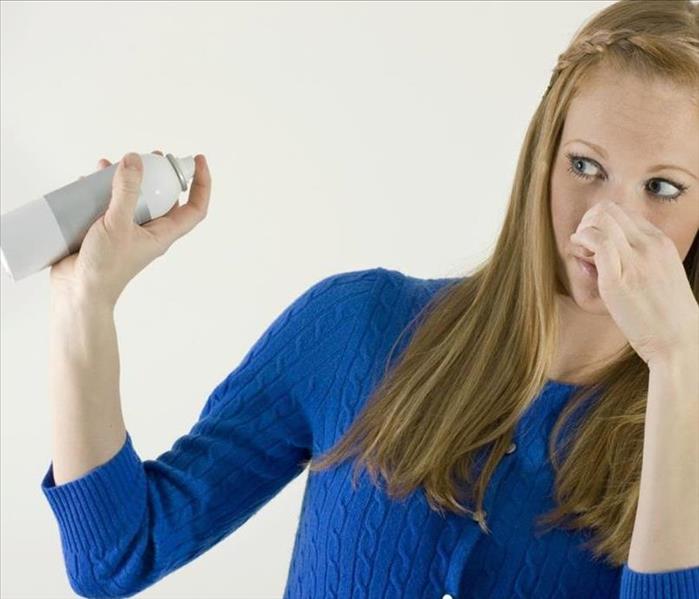 Women pinching her nose while spraying deodorizer. 