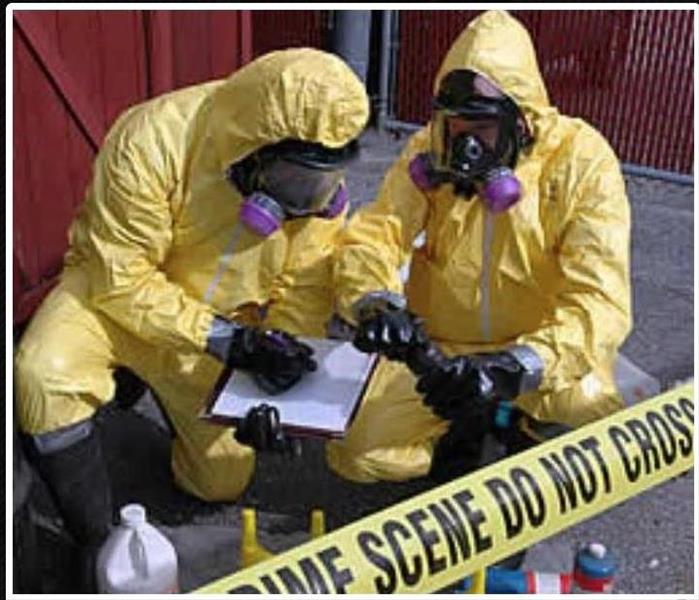 Two technicians with yellow suits and masks collecting samples with a caution tape surrounding them