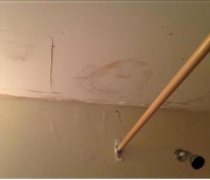 Water stained ceiling with a shower head and a old curtain metal rod attached to the wall